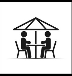 Two People Sitting At A Table Under An Umbrella